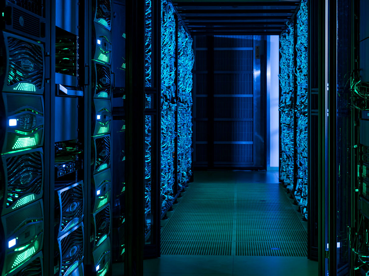 Server racks in a data center with blue-green lighting and cooling fans.