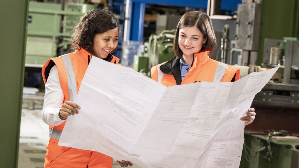 Technische Infrastruktur am KIT: Zwei Ingenieurinnen in orange Warnwesten prüfen gemeinsam einen technischen Plan.n.