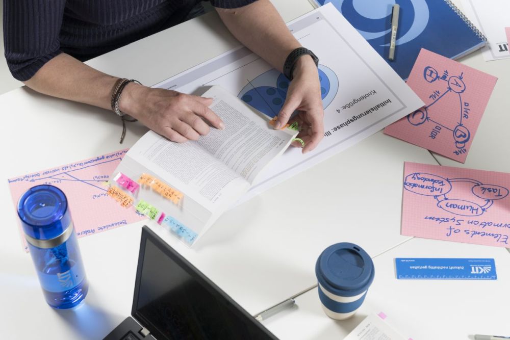 Abschlussarbeit schreiben: Student liest Dokument am Schreibtisch mit Notizen und Laptop