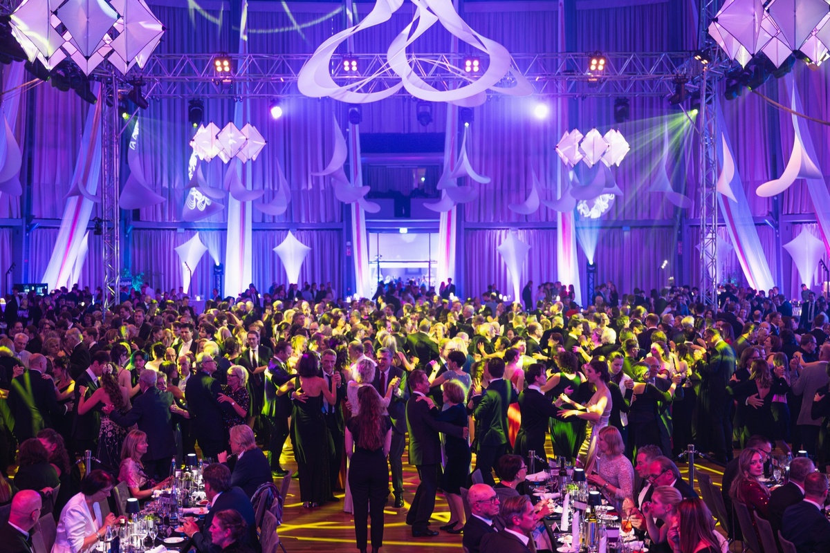 Große Gruppe elegant gekleideter Menschen tanzt und feiert in festlich dekoriertem Saal.