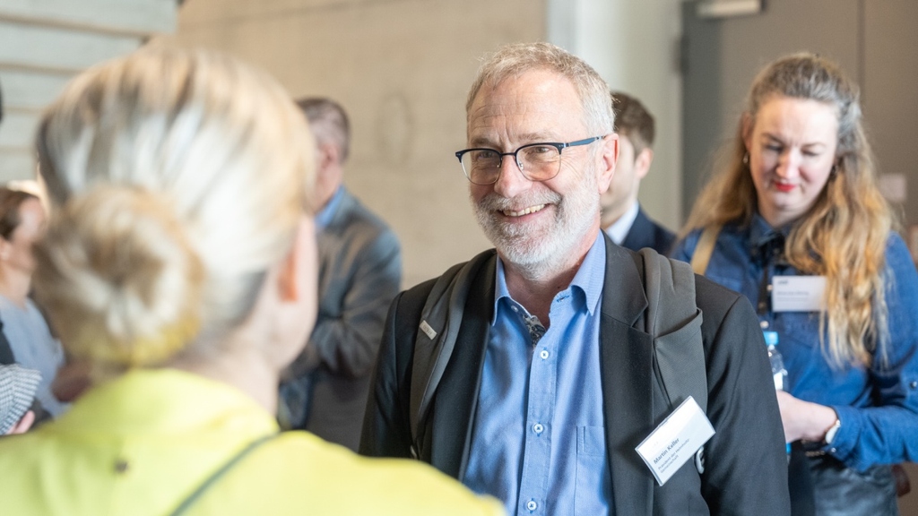 Martin Keller spricht mit einer Wissenschaftlerin, die mit dem Rücken zur Kamera steht.