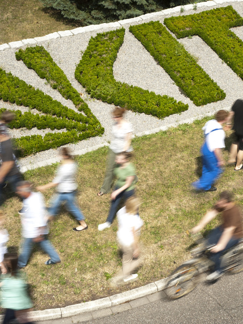 Menschen gehen an grünem KIT-Logo im Beet vorbei.