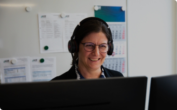 Eine Person mit Headset, die lächelnd auf zwei Monitore schaut.