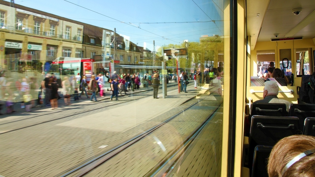 Blick aus einer Straßenbahn auf wartende Menschen an einer Haltestelle.