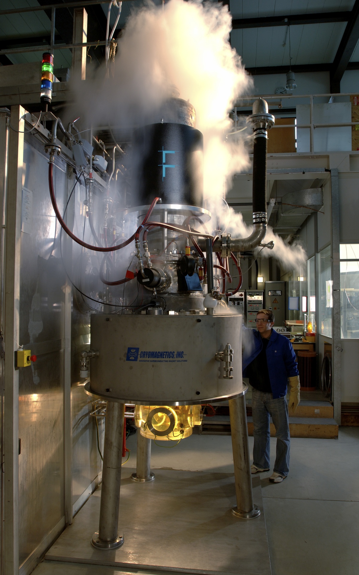 Ein Mann mit Schutzhandschuhen und Schutzbrille steht neben einem rund vier Meter hohen Ger&auml;t, aus dem es stark herausdampft.