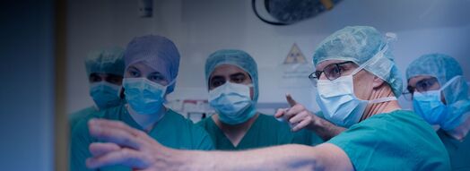 Medizinisches Team und Studierende des KIT in OP-Kleidung blicken konzentriert auf einen Bildschirm.