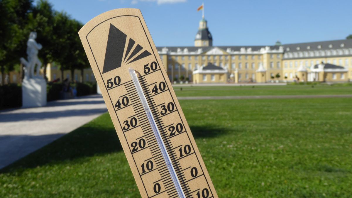 Im Vordergrund ein Thermometer, das eine Temperatur von fast 35 Grad Celsius anzeigt, im Hintergrund das Karlsruher Schloss