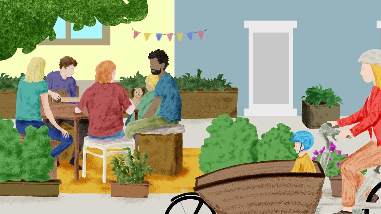 Outdoor gathering with people at a table and a cyclist with a child in a bike seat.