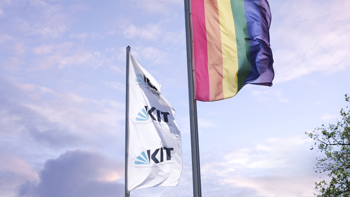 An zwei nebeneinanderstehenden Fahnenmasten wehen die Flagge des KIT und die Regenbogenflagge.