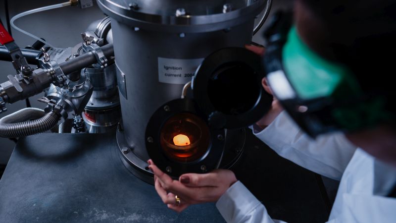 Entwicklung von Hochtemperaturverbundwerkstoffen: Wissenschaftler in Schutzkleidung betrachtet glühendes Material in einer Vakuumkammer.