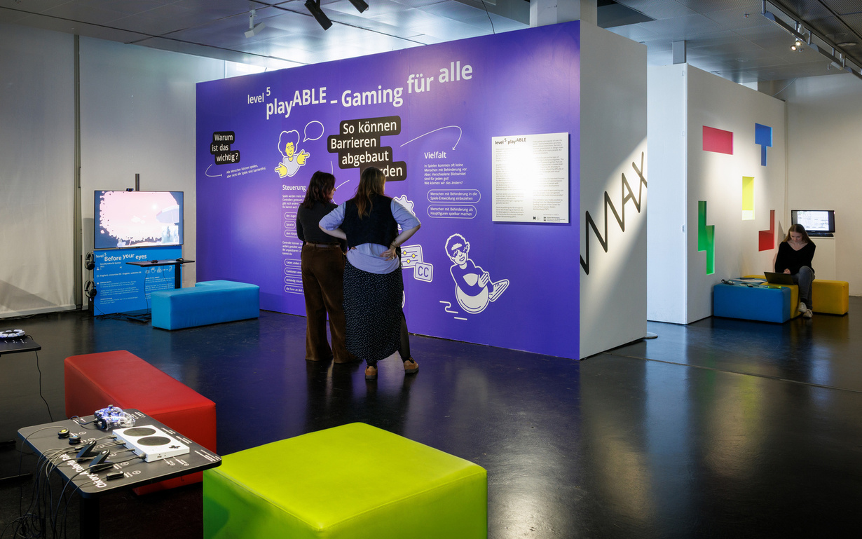 Zwei Personen betrachten eine Wand auf der steht "playABLE - Gaming für alle. So können Barrieren abgebaut werden