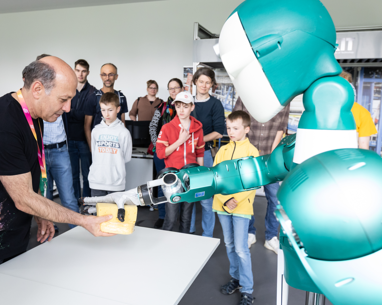 Eine Gruppe Kinder beobachtet einen Roboter in Interaktion mit einem Mitarbeiter des Reallabors