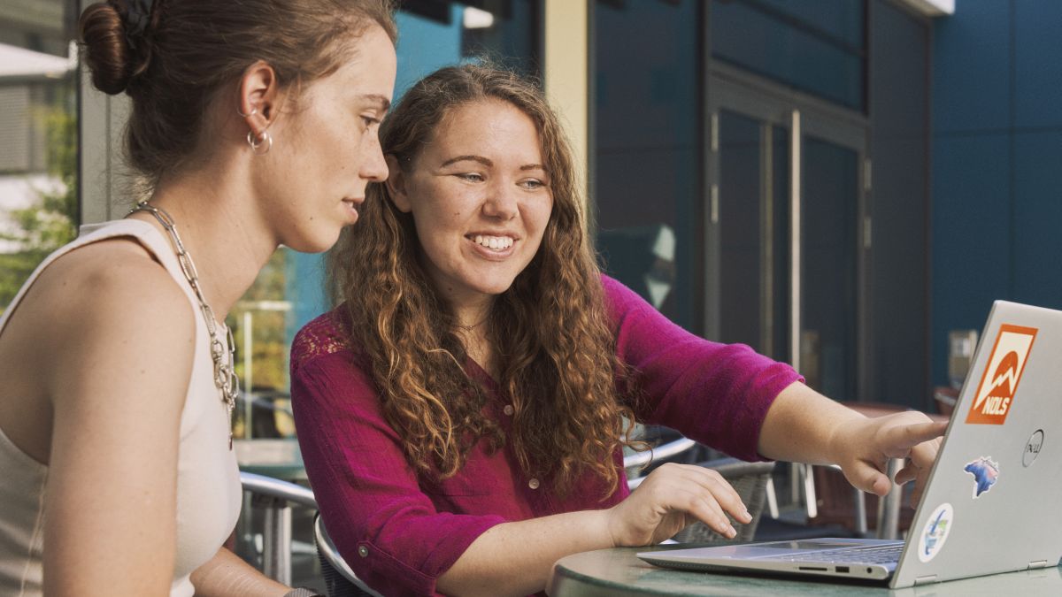 Zwei junge Studentinnen arbeiten gemeinsam an einem Laptop.