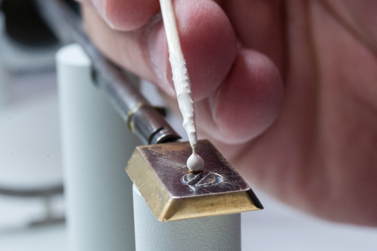 Ein Tropfen des weißen Zementleims wird auf einen messingfarbenen Metallträger geträufelt.