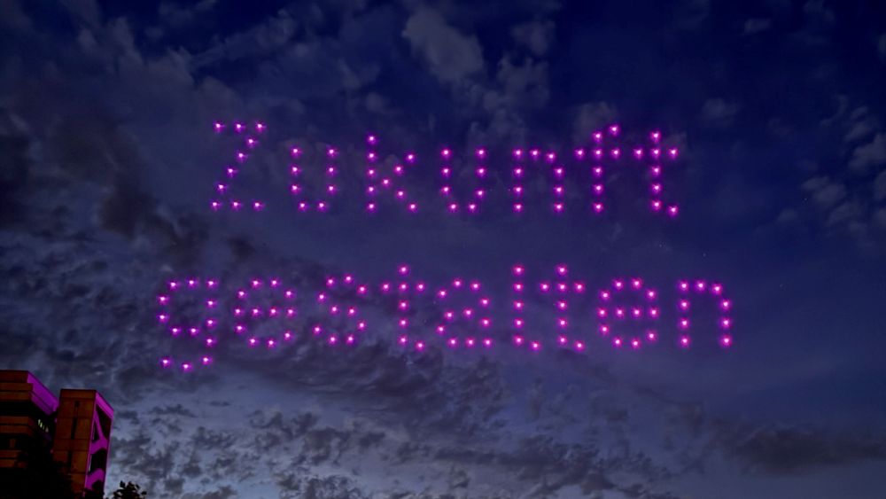 Lichtdrohnen mit dem Schriftzug "Zukunft gestalten" vor einem wolkigen Nachthimmel.